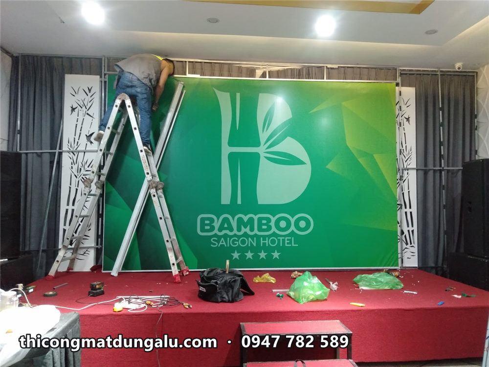 Thợ đứng trên thang nhôm căn chỉnh phông xanh in logo Bamboo trên sân khấu thảm đỏ