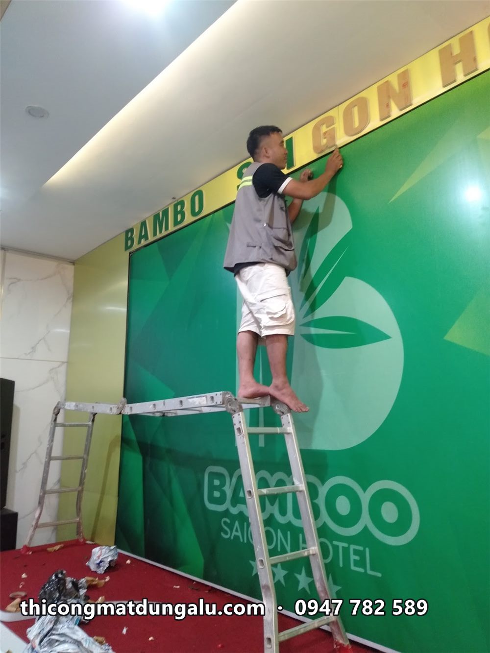 Thợ đứng trên thang gắn chữ nổi Bamboo Saigon Hotel lên tường phía trên phông xanh