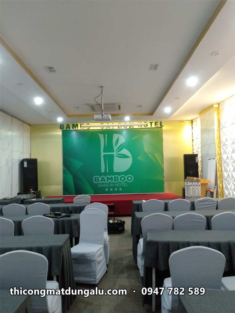 Phòng hội nghị khách sạn xếp bàn ghế bọc trắng hướng về backdrop xanh