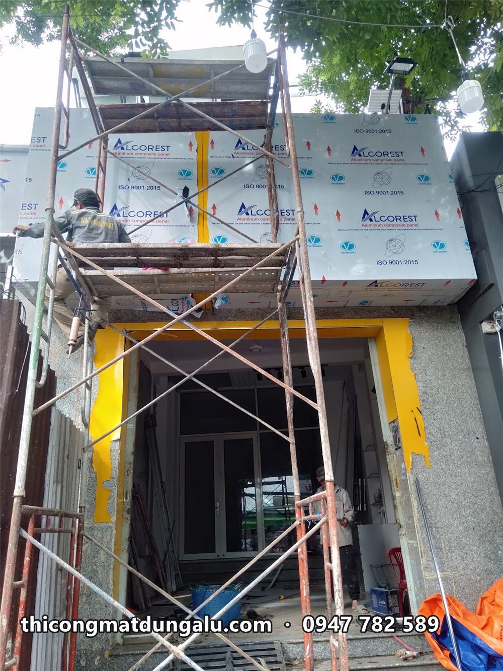 Thợ trên giàn giáo ốp tấm alu lên khung mặt tiền, hai trụ cửa đã ốp alu vàng