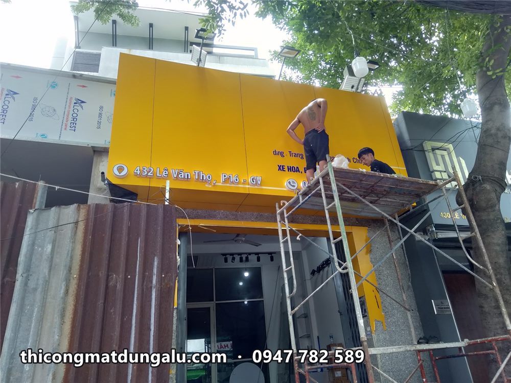 Thợ trên giàn giáo gắn chữ lên mặt biển alu vàng