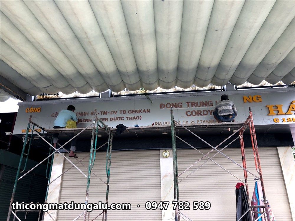 Thợ trên giàn giáo lắp bảng hiệu ngay dưới mái tôn, trước cửa cuốn