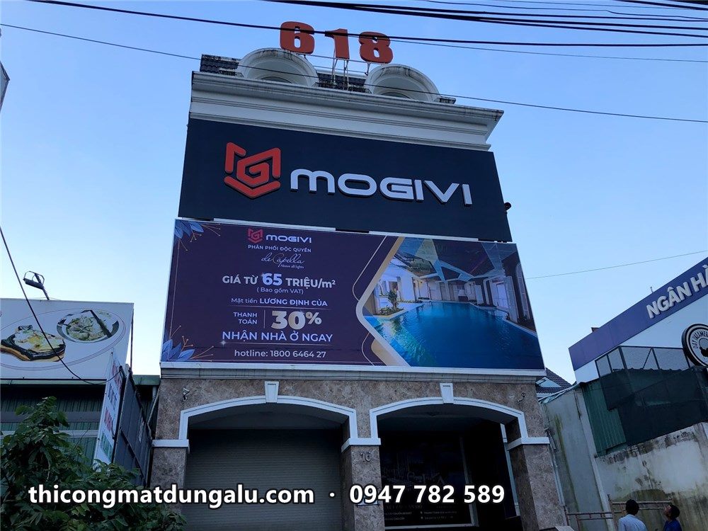 Mặt tiền tòa nhà với bảng Mogivi và bạt dự án nhìn từ dưới lên