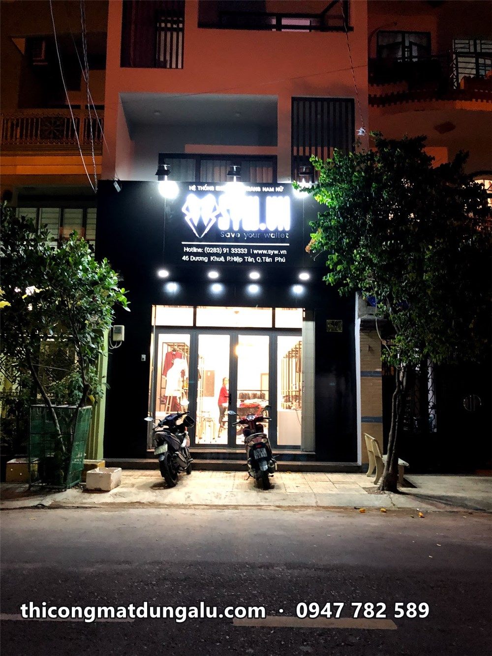 Shop SYW ban đêm, mặt tiền đen và đèn chiếu rọi xuống cửa