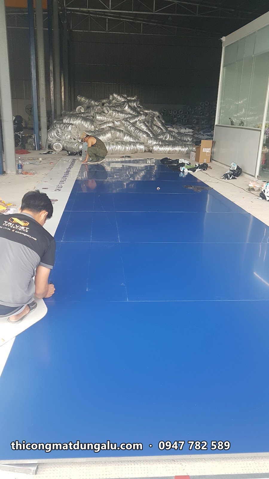 Thợ trải tấm alu xanh dương khổ lớn trên sàn xưởng