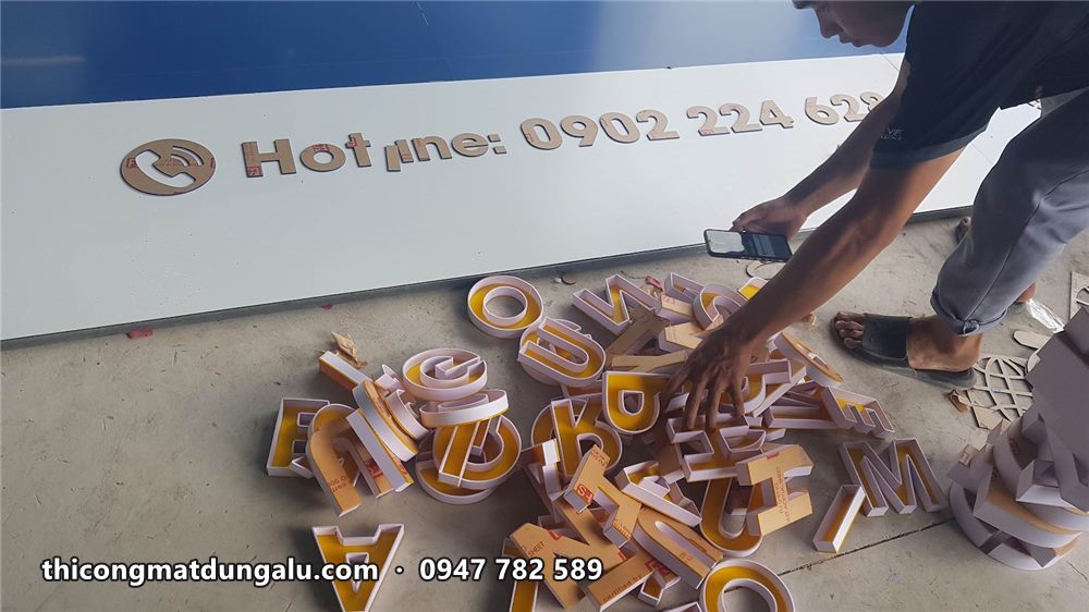 Thợ sắp xếp các chữ nổi vàng trên sàn cạnh dải số điện thoại hotline