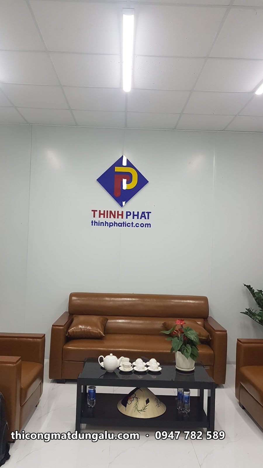 Logo Thịnh Phát chữ nổi trên tường trắng phòng tiếp khách, sofa da nâu phía dưới