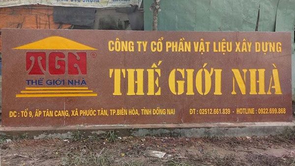 Bảng hiệu công ty vật liệu xây dựng Thế Giới Nhà chữ vàng trên nền đá đỏ nâu, logo mái nhà