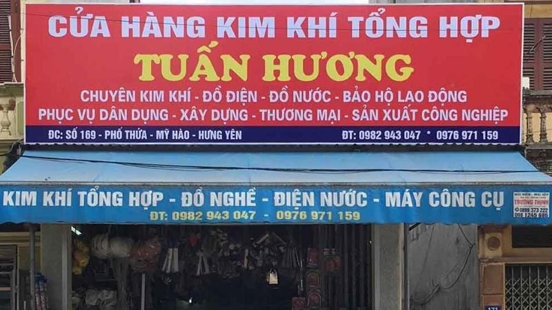Bảng hiệu cửa hàng kim khí tổng hợp nền đỏ chữ vàng, mái hiên xanh in dòng phụ
