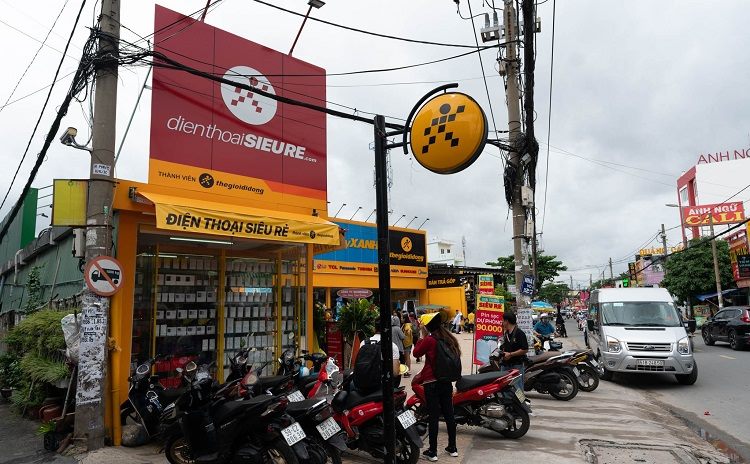 Cửa hàng điện thoại ở góc đường với trụ bảng hiệu cao, nền đỏ và logo