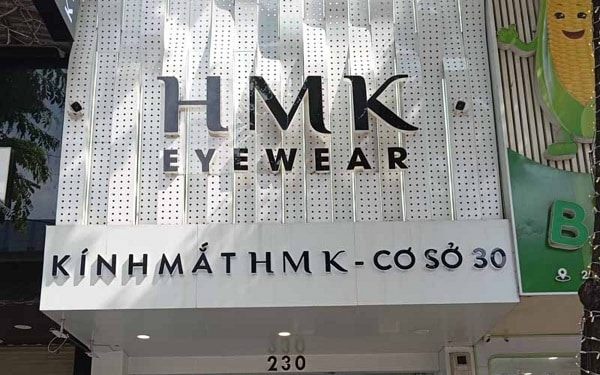 Mặt tiền tiệm kính mắt HMK Eyewear ốp alu đục lỗ trắng, chữ nổi xám mảnh