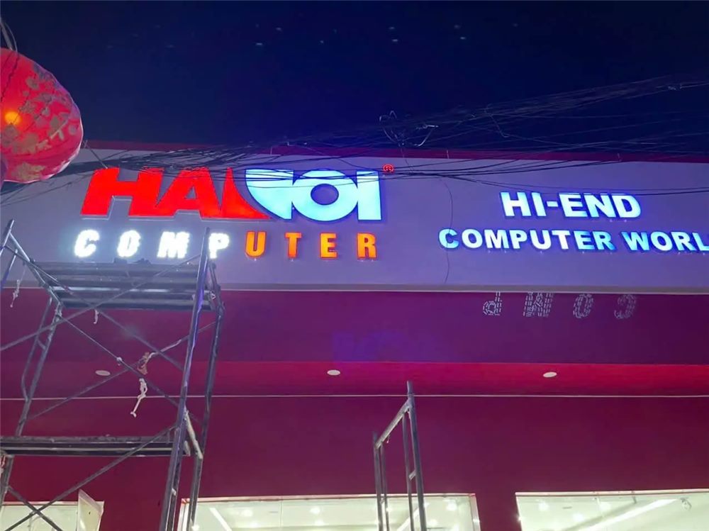 Cận cảnh chữ nổi phát sáng tên cửa hàng máy tính trên nền đỏ ban đêm