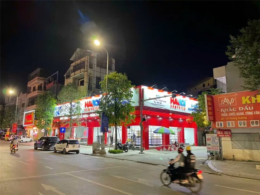 Toàn cảnh cửa hàng máy tính góc phố ban đêm với mặt dựng đỏ sáng đèn