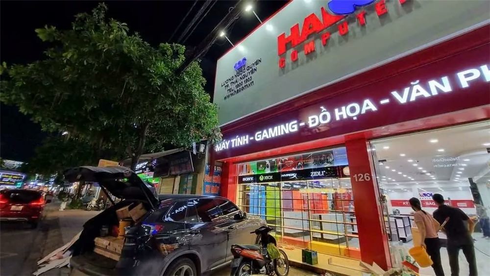 Mặt tiền cửa hàng máy tính ban đêm với dòng chữ ngành hàng và cửa kính lớn
