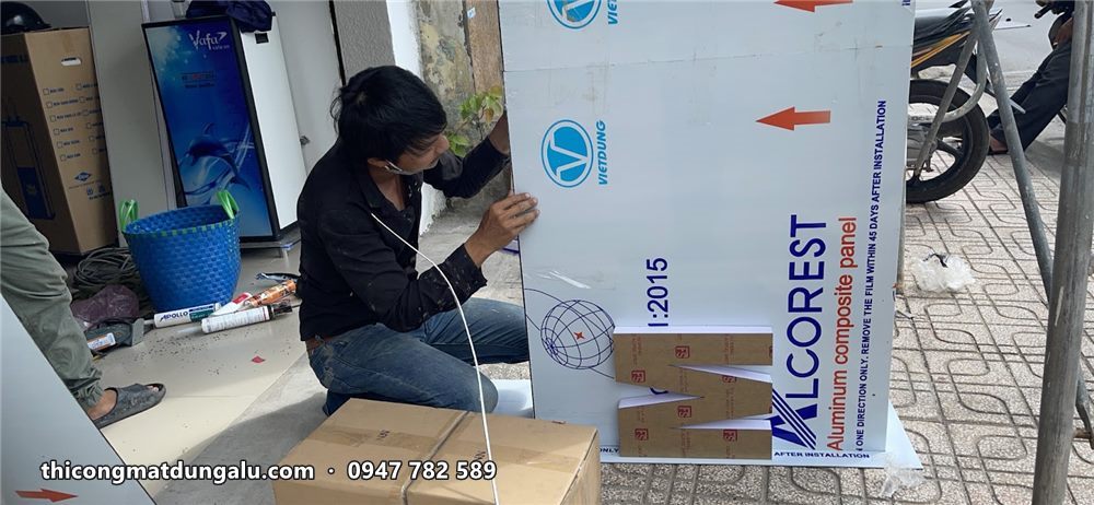 Thợ gia công biển alu trắng xanh trên vỉa hè, tấm alu Alcorest còn màng