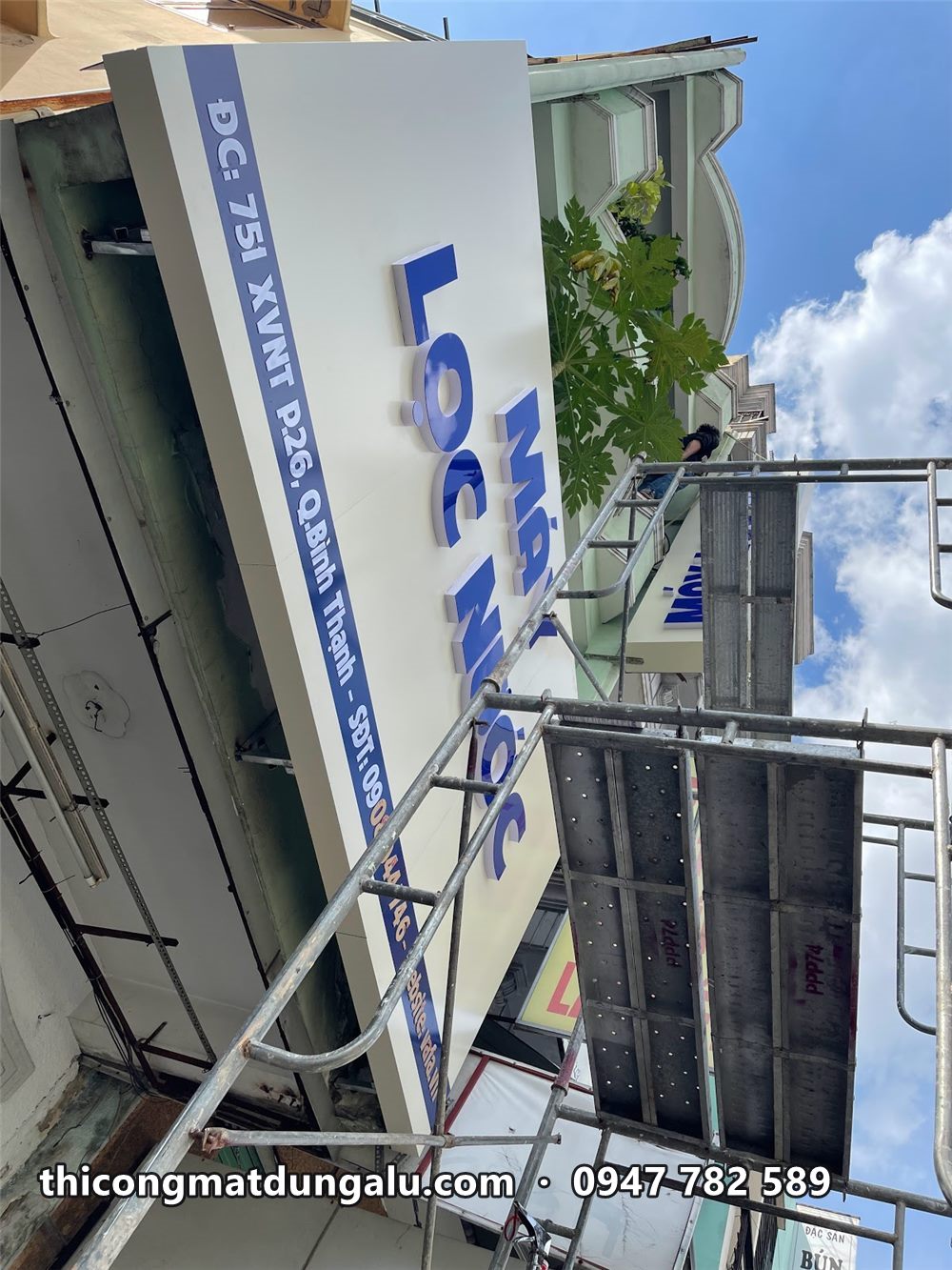 Biển dọc Máy Lọc Nước chữ xanh trên khung sắt, nhìn từ dưới lên