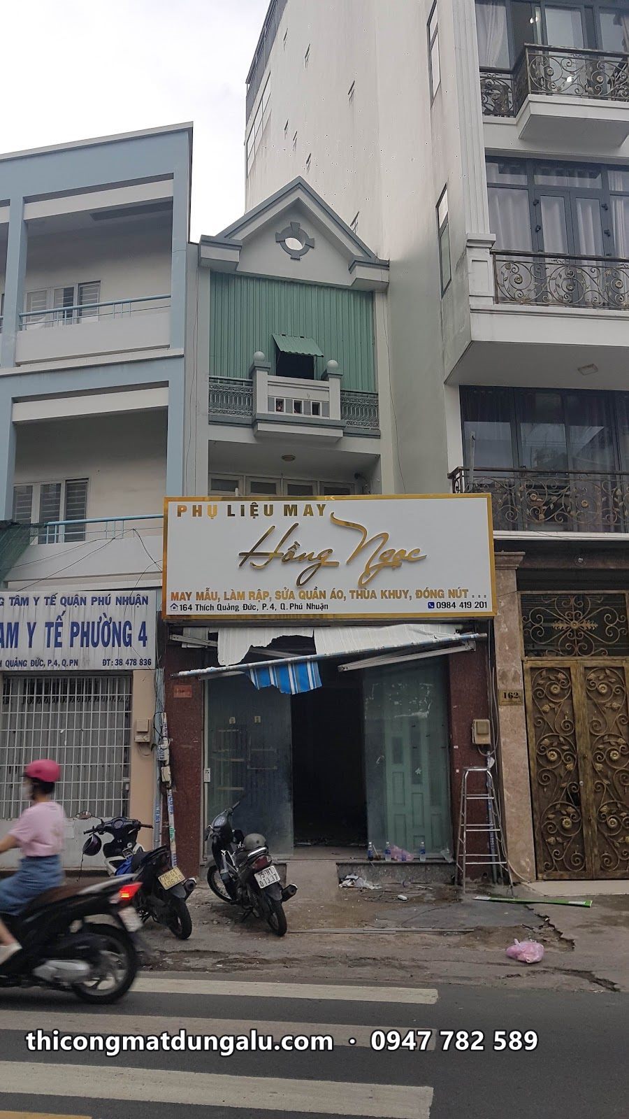 Nhà phố nhiều tầng với biển ngang chữ vàng trên nền kem ở tầng trệt