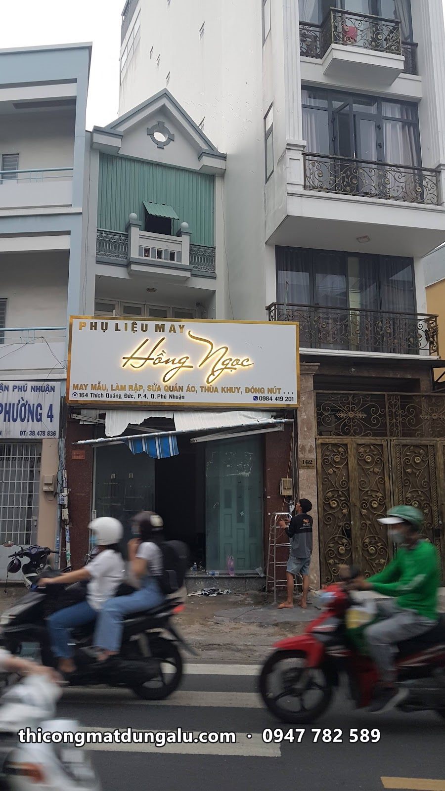 Biển chữ vàng trên mặt tiền nhà phố, xe máy chạy qua phía trước