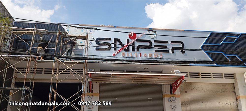 Thợ trên giàn giáo lắp bảng hiệu Sniper chữ trắng nền đen trên cửa hàng