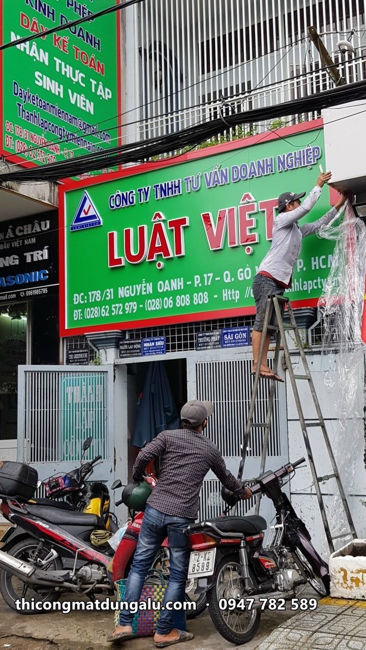 Thợ lắp biển Luật Việt nền xanh lá chữ đỏ trên mặt tiền nhà phố