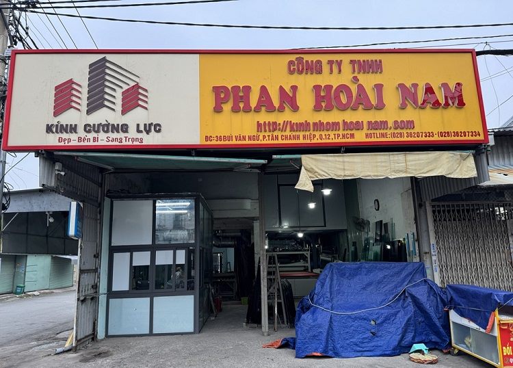 Bảng hiệu công ty kính cường lực nền vàng chữ đỏ, khối logo tòa nhà bên trái