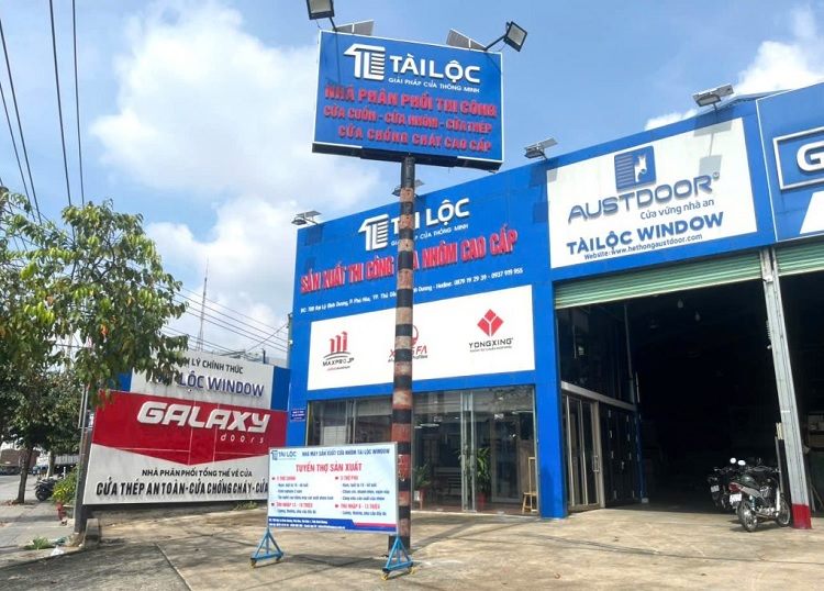 Cửa hàng nhôm kính mặt dựng xanh dương cao, bảng trên cột trụ và logo hãng cửa