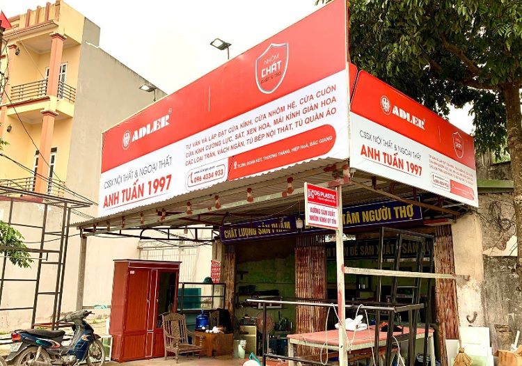 Cửa hàng nhôm kính với bảng hiệu trắng đỏ và logo hãng ở hai đầu