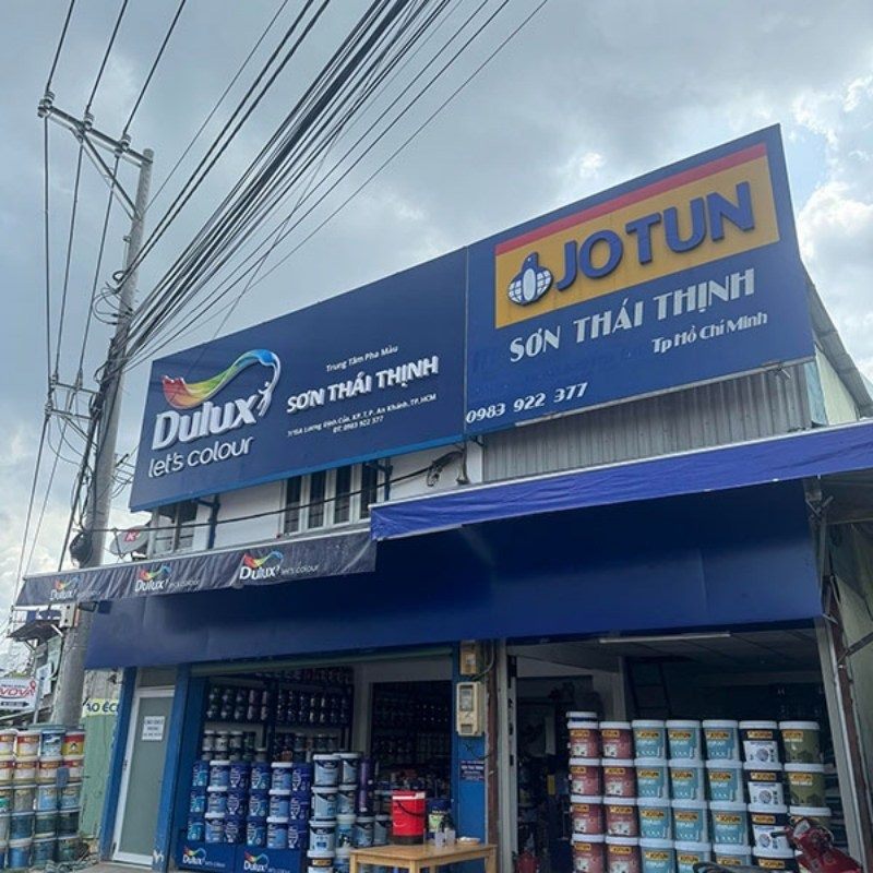 Cửa hàng sơn Thái Thịnh với bảng Dulux, Jotun xanh dương chạy dài trên mái hiên