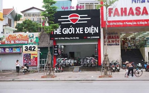 Cửa hàng Thế giới xe điện bảng đen, logo đỏ, chữ nổi trắng và xe xếp kín vỉa hè