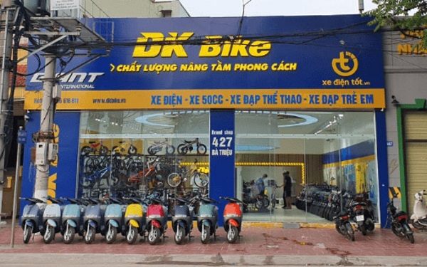 Cửa hàng DK Bike bảng xanh dương, chữ nổi vàng và dải dịch vụ, xe xếp phía trước