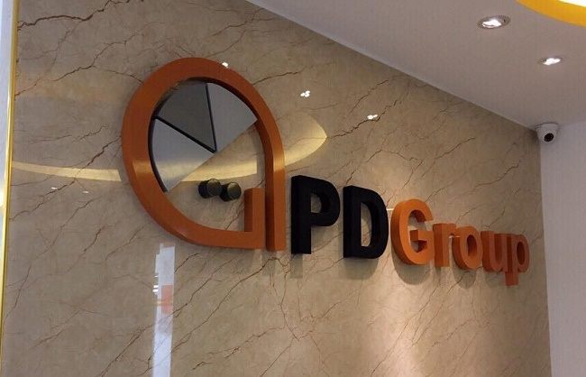 Logo chữ nổi cam và đen gắn trên tường đá vân sáng ở sảnh văn phòng