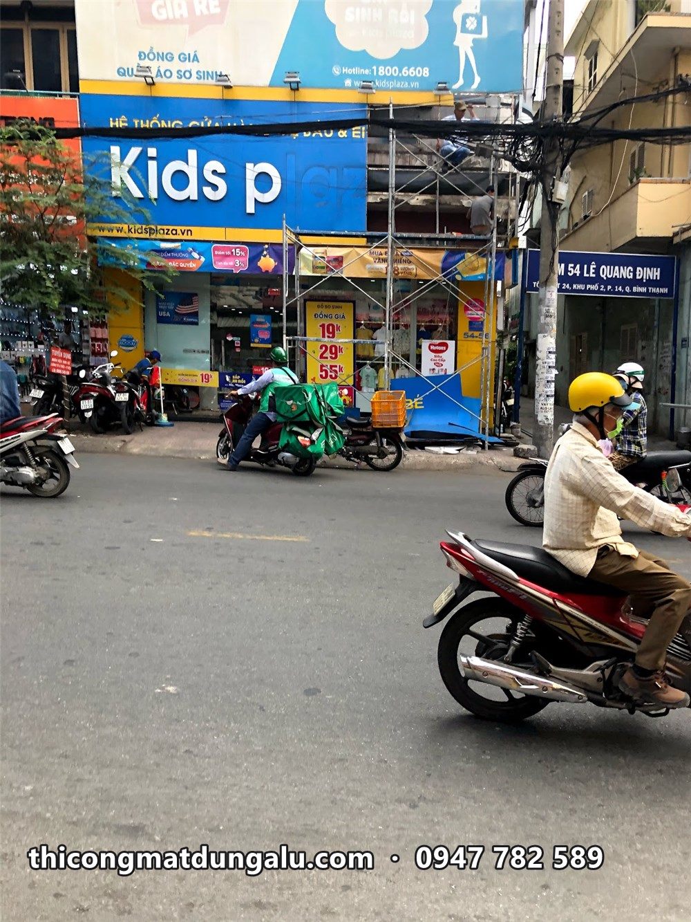 Giàn giáo trước cửa hàng KidsPlaza ở góc phố, xe máy chạy qua