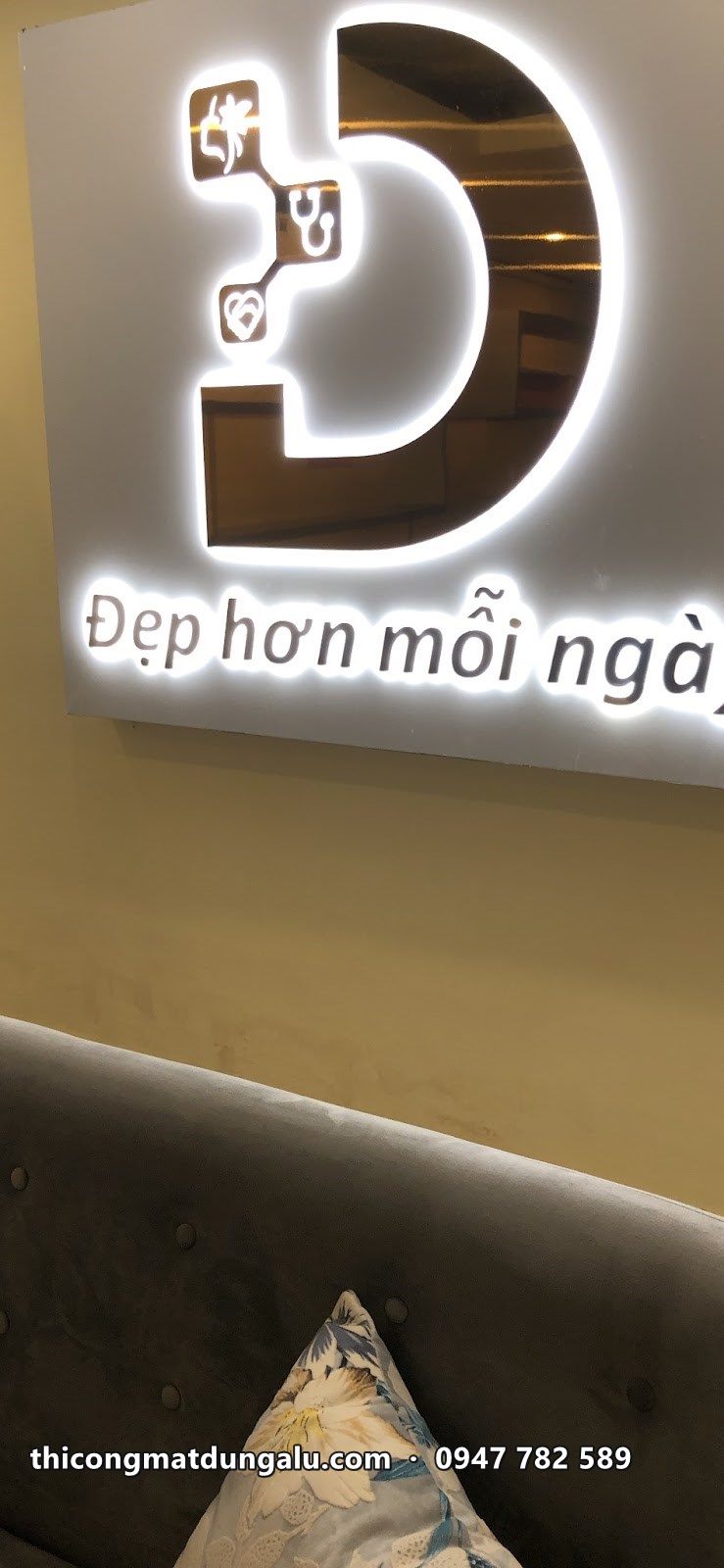 Logo chữ D vàng hắt sáng với dòng Đẹp hơn mỗi ngày trên vách trong phòng khám
