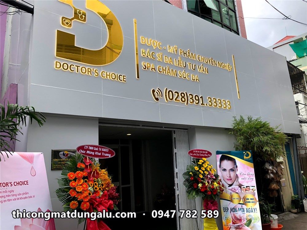 Mặt tiền phòng khám Doctor's Choice nền alu xám, logo D vàng, lẵng hoa khai trương