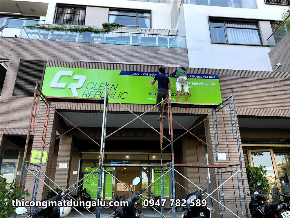 Thợ trên giàn giáo lắp biển Clean Republic xanh chanh trên lối vào tòa nhà