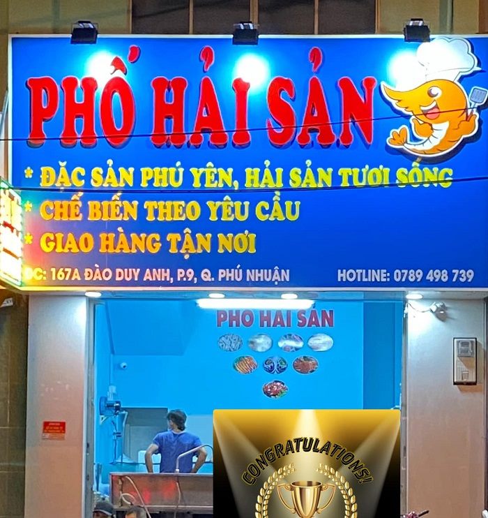 Bảng hiệu quán hải sản nền xanh, chữ nổi đỏ vàng và đèn pha