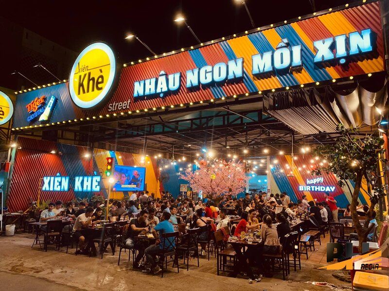 Quán nhậu sân rộng với bảng hiệu nhiều màu, chữ nổi và dây đèn