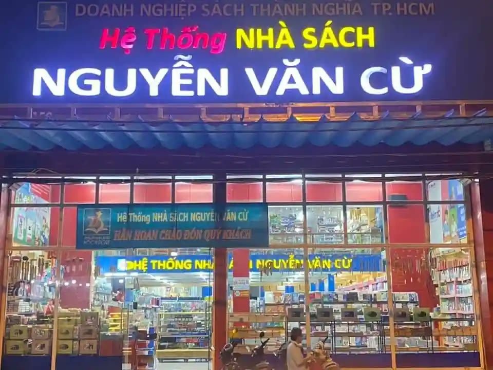 Nhà sách về đêm với bảng xanh tím, chữ nổi trắng phát sáng và mặt kính đầy kệ hàng