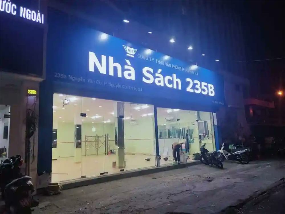 Nhà sách mới về đêm với bảng xanh dương, chữ nổi trắng và mặt kính chưa trưng bày