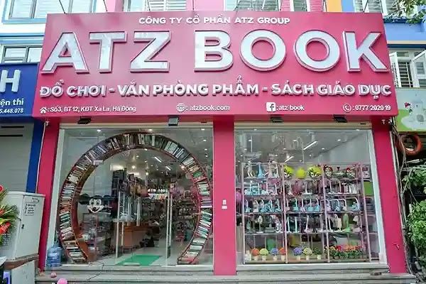 Cửa hàng ATZ Book bảng hồng, chữ nổi trắng lớn và cửa kính trưng bày đồ chơi