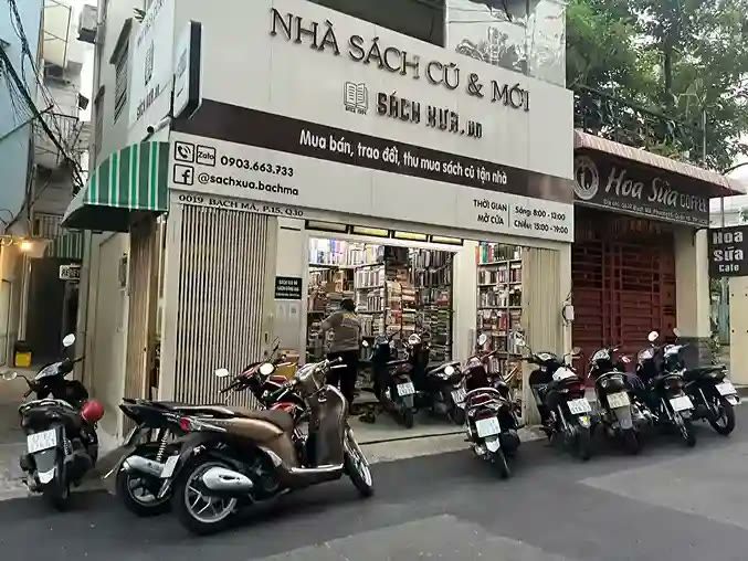 Nhà sách cũ và mới với bảng trắng chữ đen ở góc phố, xe máy đậu phía trước