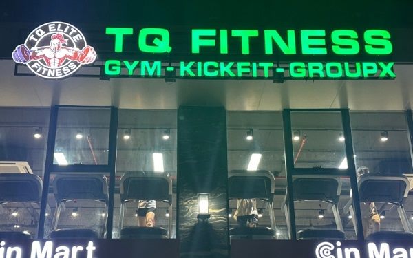 Bảng hiệu fitness chữ xanh neon sáng trên mặt kính nhiều tầng