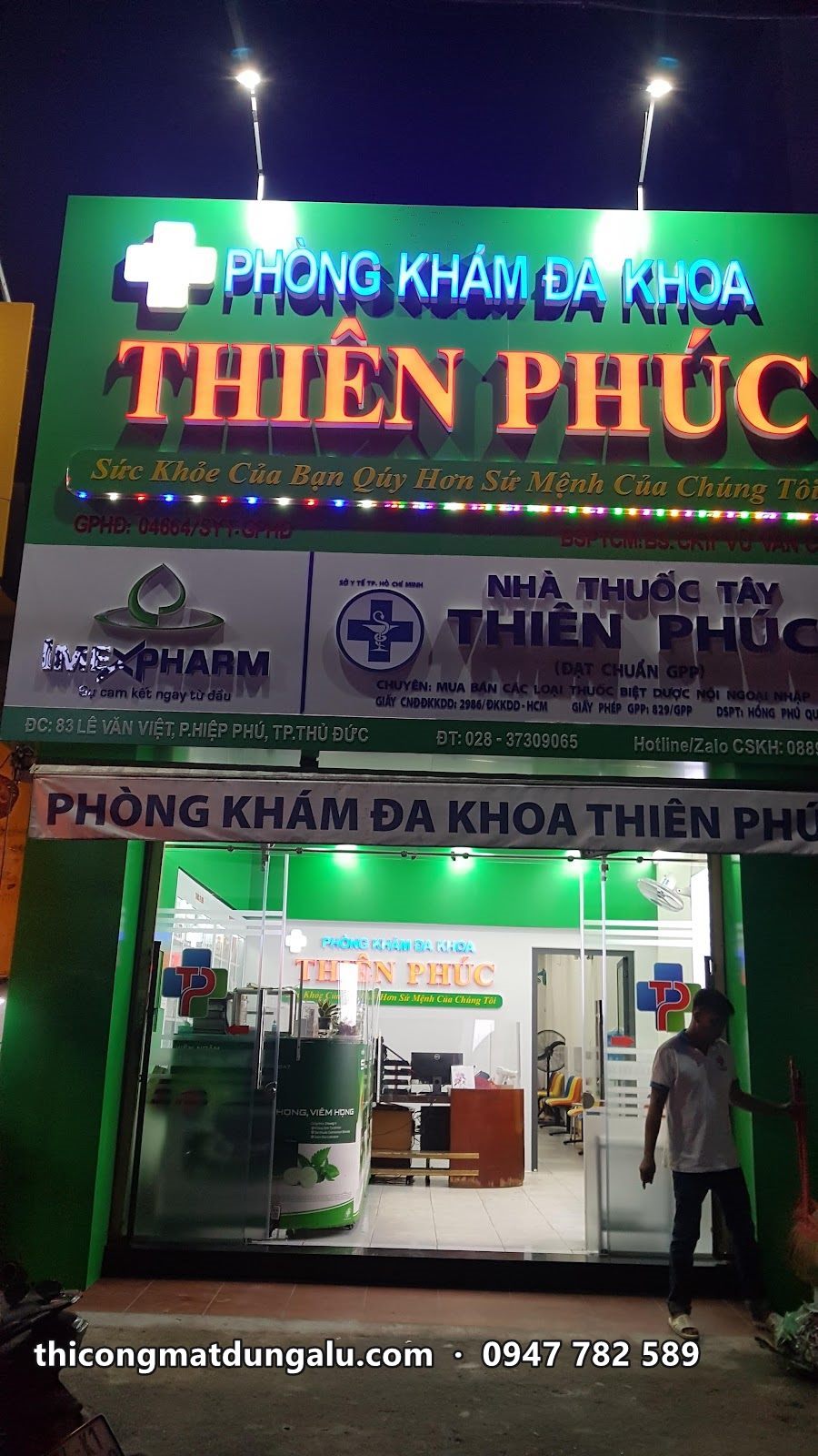 Toàn cảnh mặt tiền phòng khám về đêm với bảng tên, biển nhà thuốc và cửa kính sáng đèn