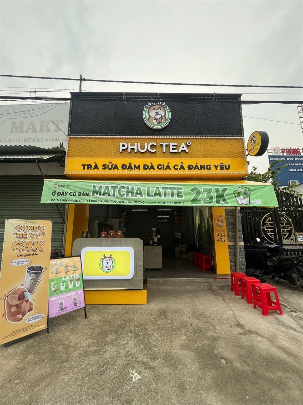 Mặt tiền quán trà sữa ốp vàng đen, logo tròn và băng rôn khuyến mãi