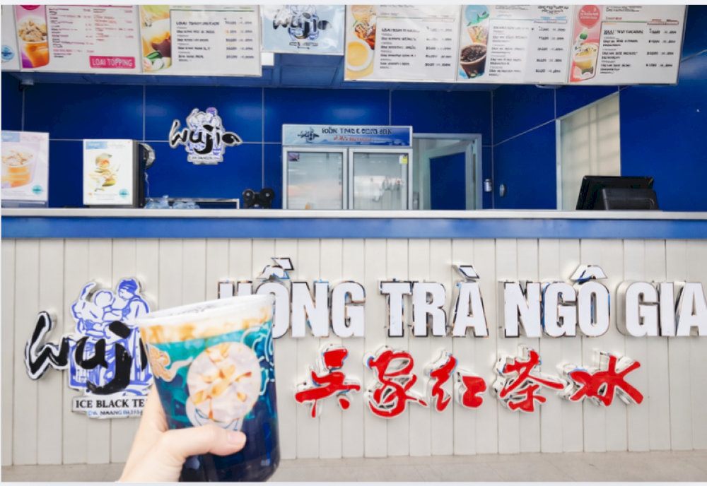Quầy order quán trà sữa ốp trắng với chữ nổi xanh đỏ và menu treo phía trên