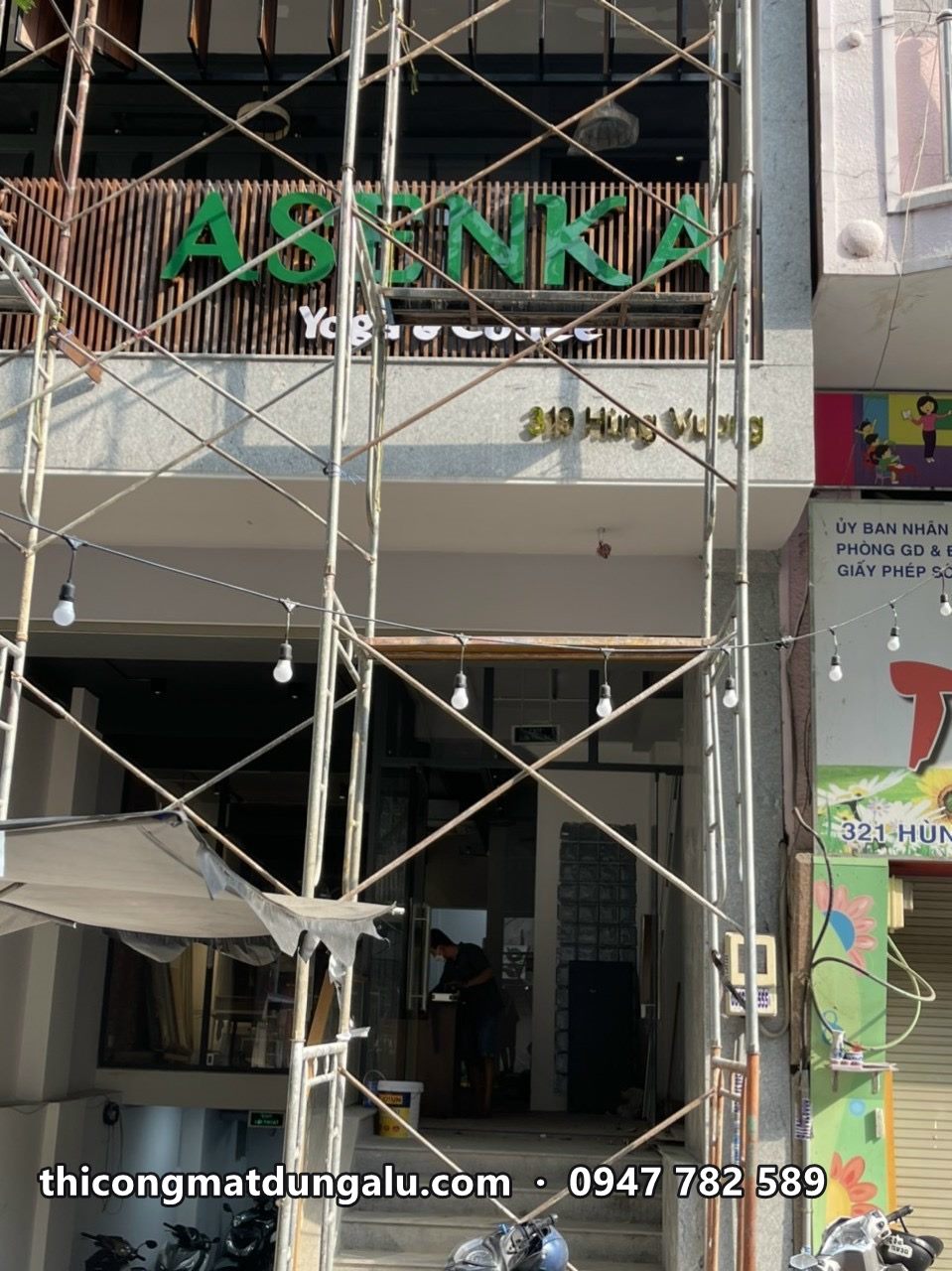 Chữ ASENKA xanh lá trên nền ốp gỗ, giàn giáo phía trước