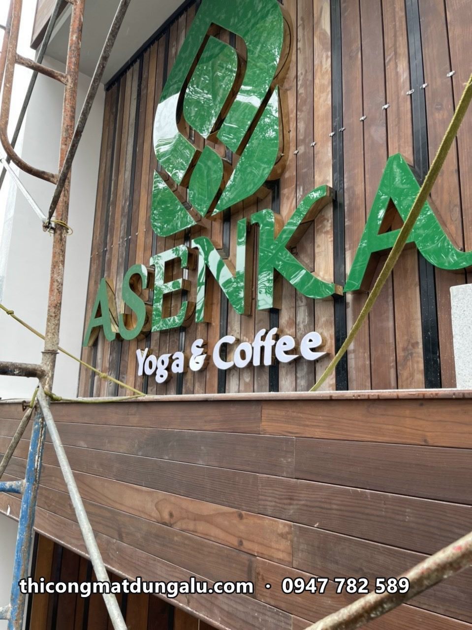 Cận cảnh logo lá xanh và chữ ASENKA Yoga and Coffee trên ốp gỗ nâu