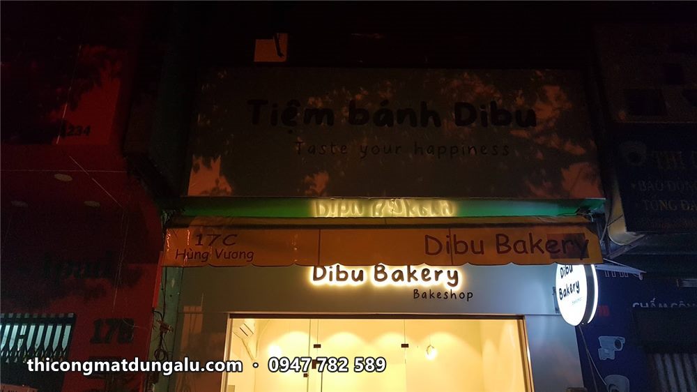 Tiệm Dibu Bakery ban đêm với chữ sáng phía trên cửa kính và quầy sáng vàng
