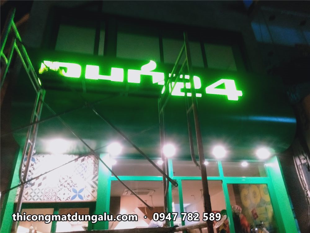 Chữ nổi xanh lá sáng đêm trên mặt tiền quán, đèn chiếu sáng phía dưới