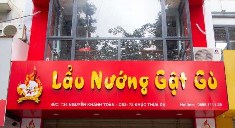 Bảng hiệu Lẩu Nướng Gật Gù nền đỏ chữ vàng, logo đầu bếp và ngọn lửa